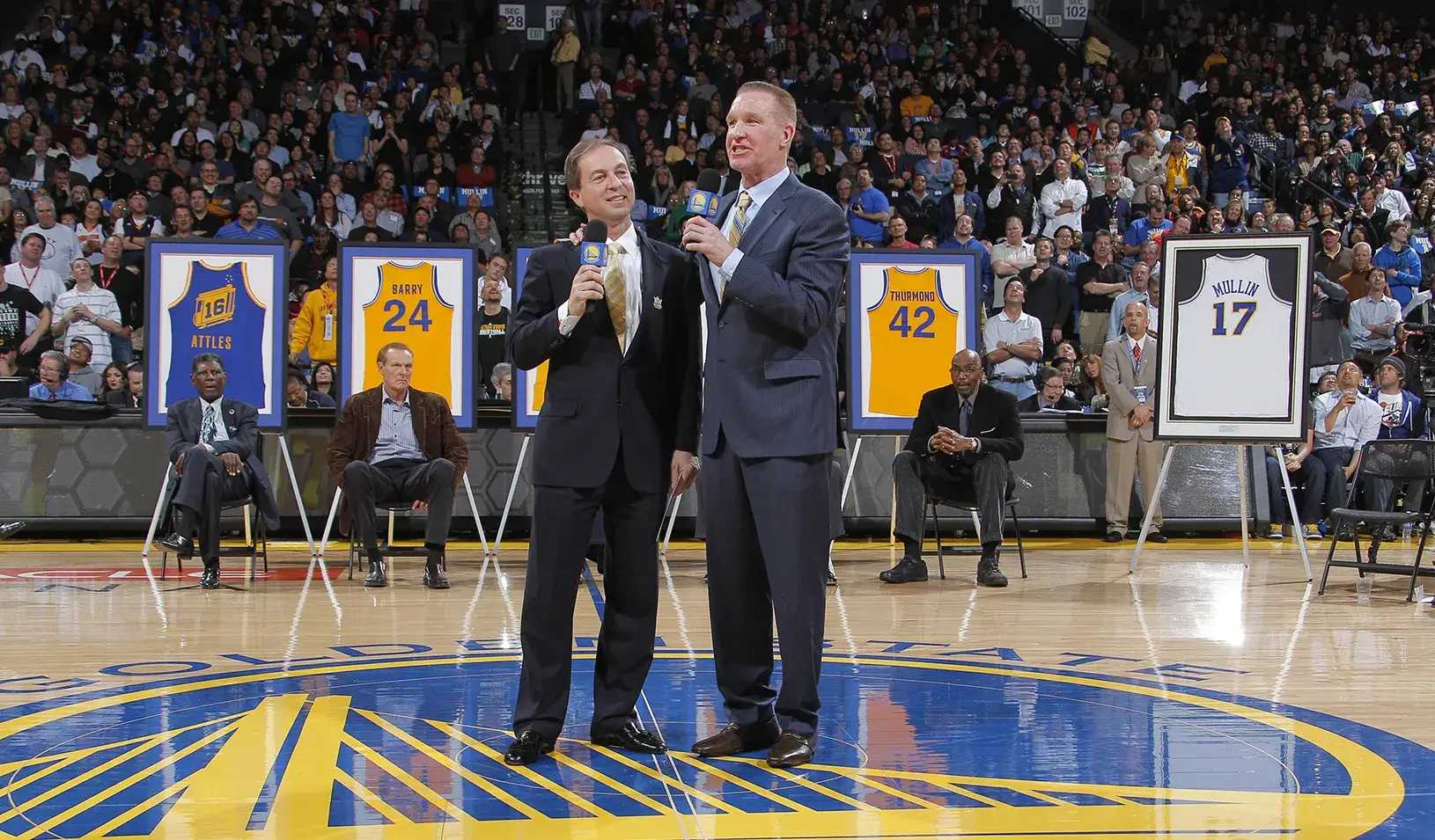 Golden State Warriors owner Joe Lacob, left, speaks with former player Chris Mullin during a ceremony to retire his #17 jersey at halftime of a game between the Warriors and Minnesota Timberwolves on March 19, 2012. Credit: Rocky Widner/NBAE via Getty Images