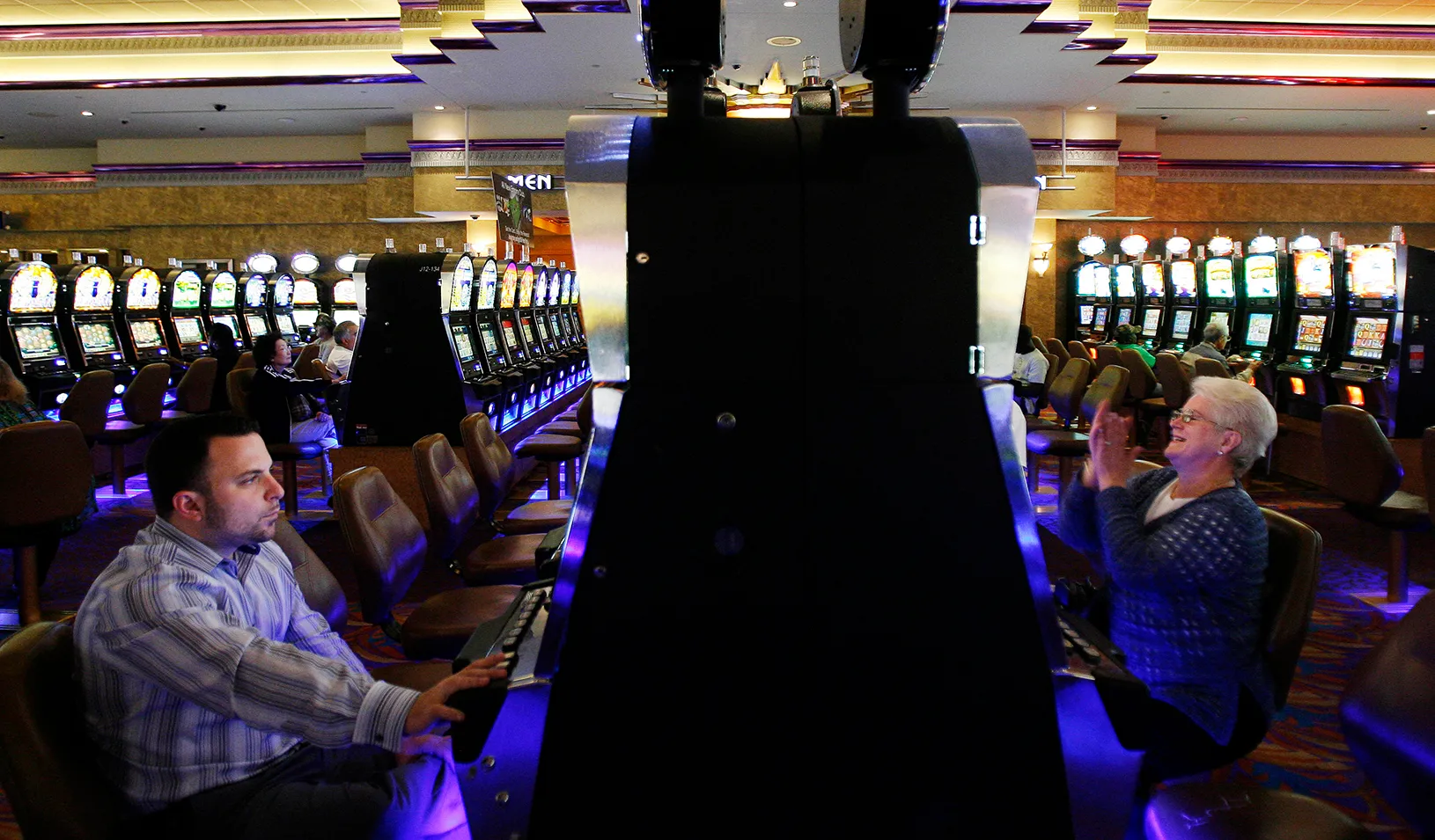 A man and a woman gambling at opposing slot machines in a casino. The woman is smiling and clapping, and the man looks focused. Credit: Reuters/Lucas Jackson