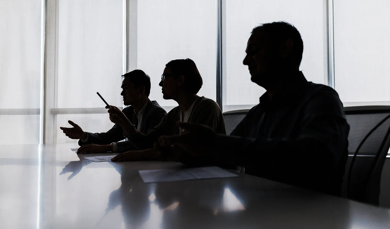 Silhouette of three board members in a dark conference room. Credit: iStock/FangXiaNuo