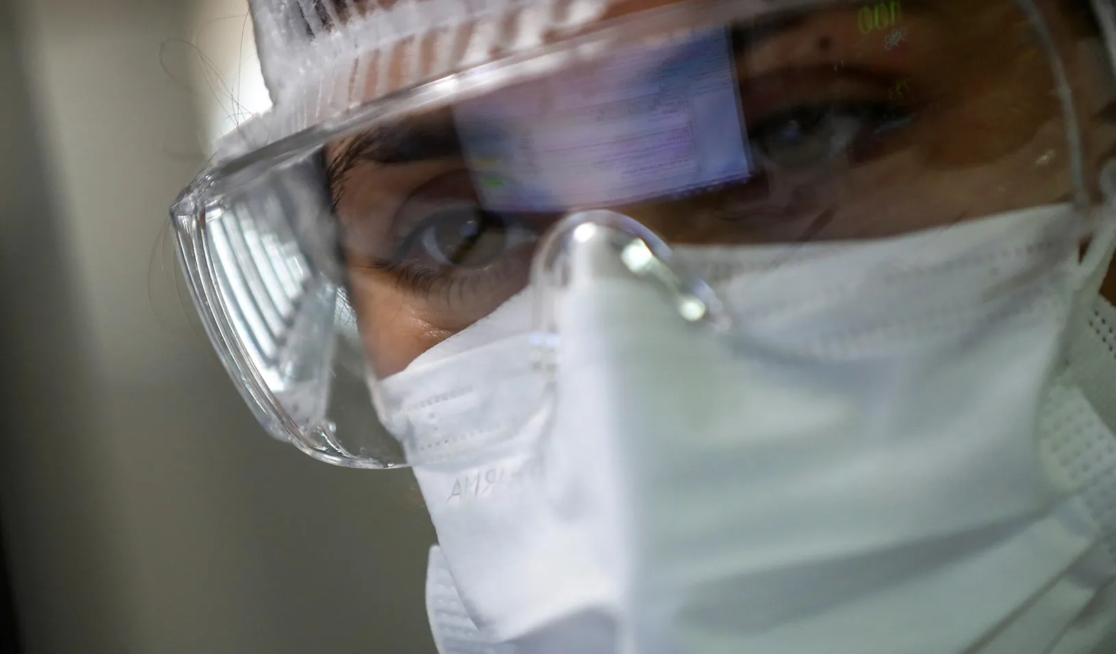 A closeup of a masked health care worker looking at a computer monitor. Photo by Reuters/Agustin Marcarian