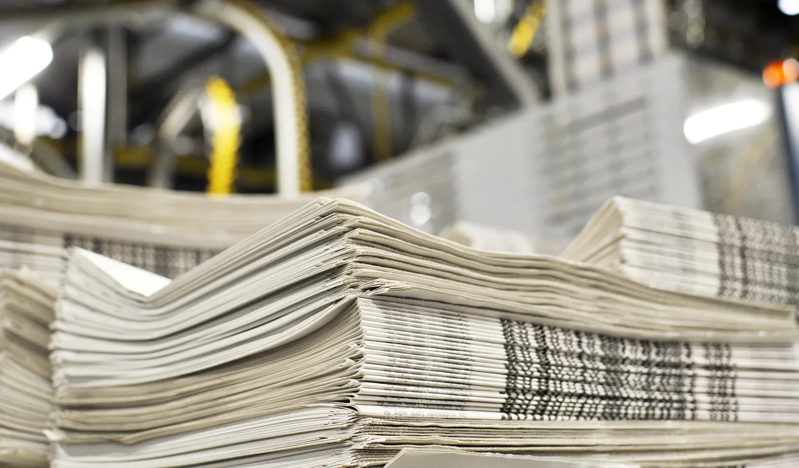 A stack of freshly printed newspapers, in the background printing machines and technical equipment. Credit: iStock/industryview