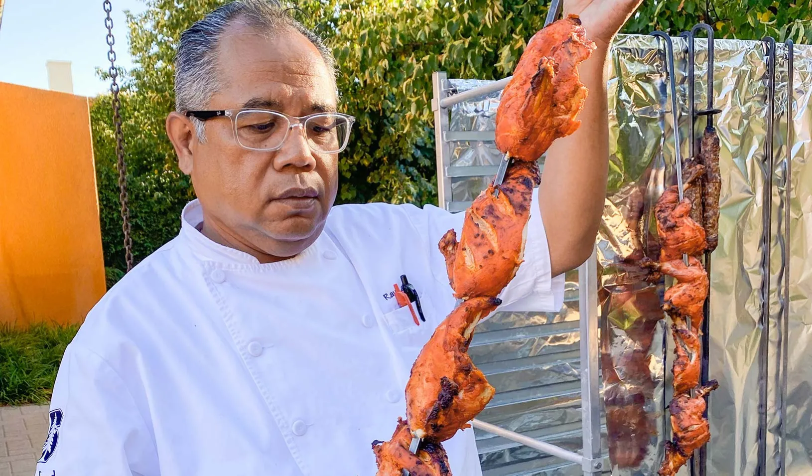 Executive Education Dining Chef Raul Lacara standing outside while holding meat on a skewer.  | Courtesy of Chef Raul Lacara.