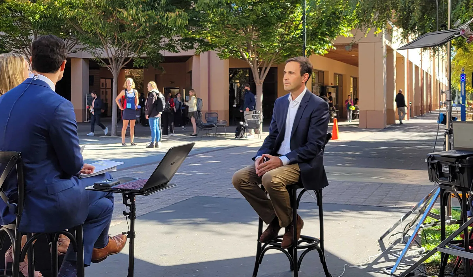 Stanford GSB dean Jonathan Levin sits outside in Town Square in front of two Bloomberg Reporters.  | Credit:  Sheila Singh.