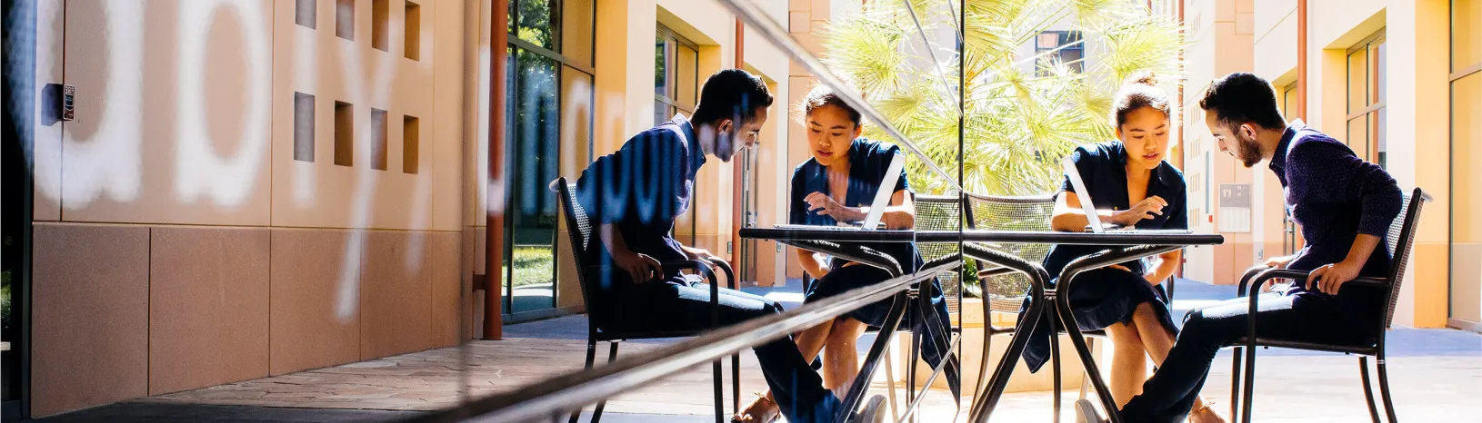 Two students looking at a laptop and sitting at a table outside on a sunny day.