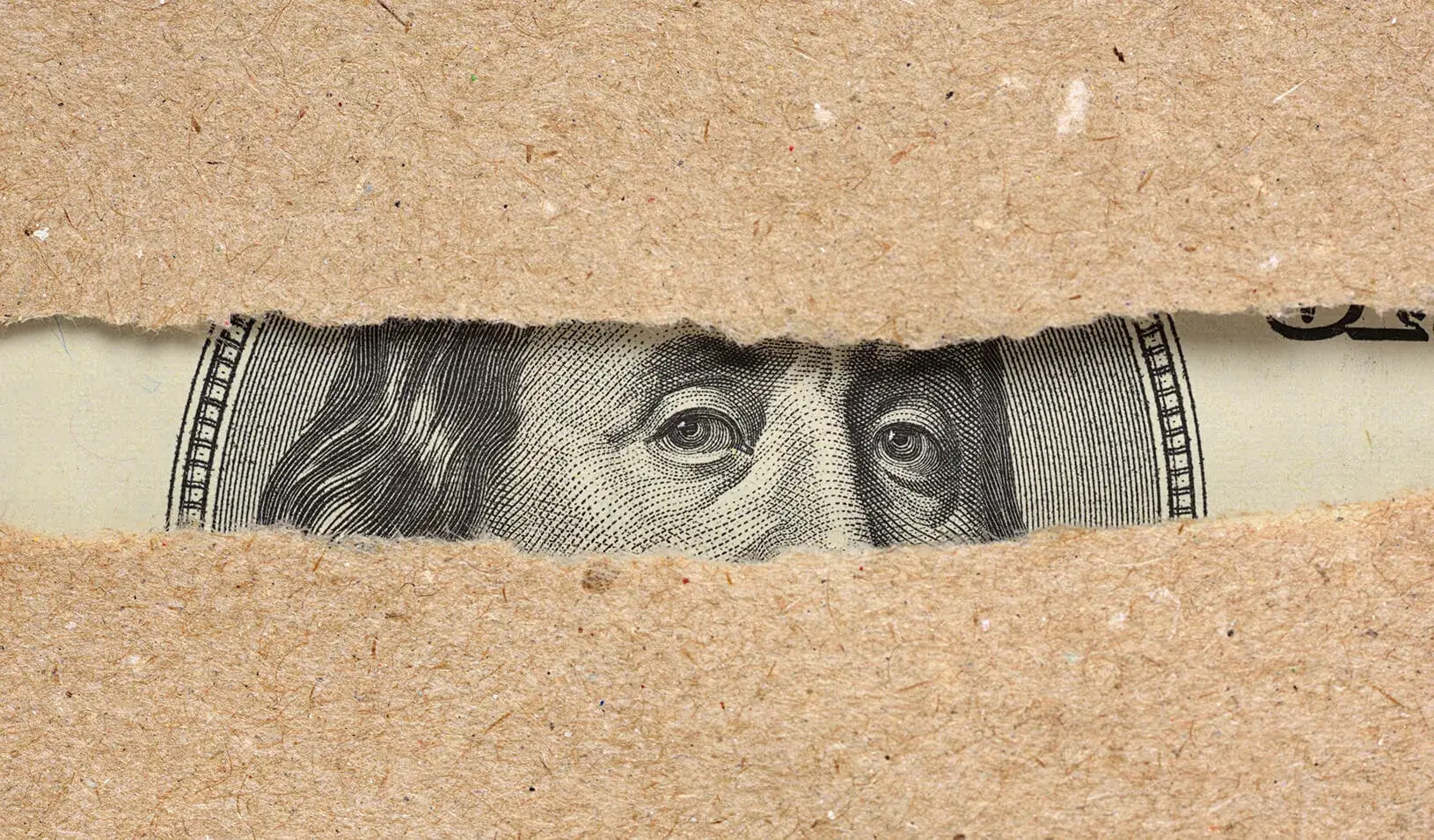 Benjamin Franklin's face from the hundred dollar bill peeking through a torn piece of paper. iStock/Kuzmik_A