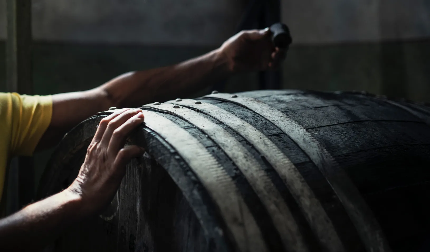 a close up photo of a man's hands doing quality control on an aging barrel. Credit: iStock/ArtistGNDphotography