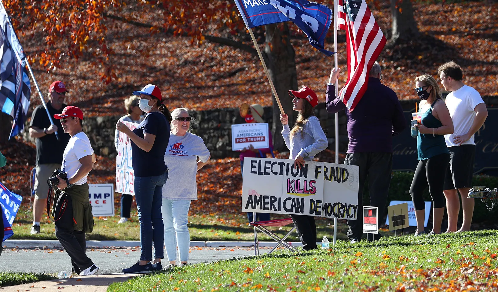 Protesters waving Trump and American flags hold a sign that reads "Election fraud kills American democracy." 