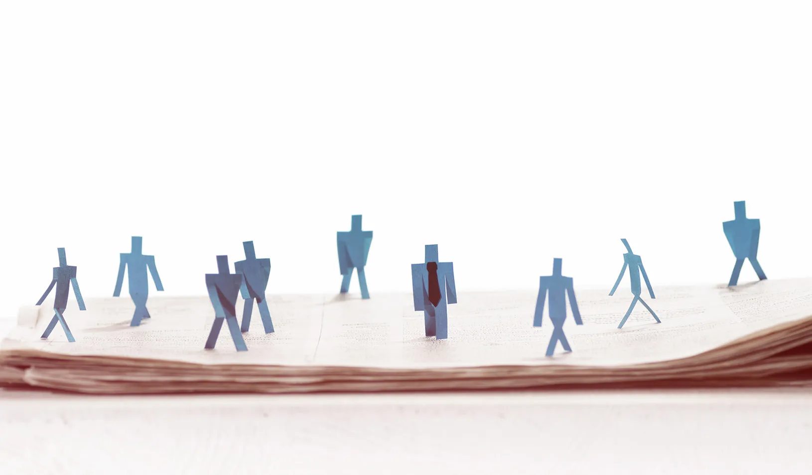 Illustration of human figures cut out of paper, following behind a leader in a suit.
