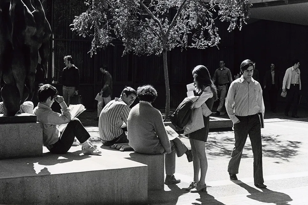 Historical black and white image from the GSB archives, showing an old photo of campus, and students milling around the The Birds sculpture.