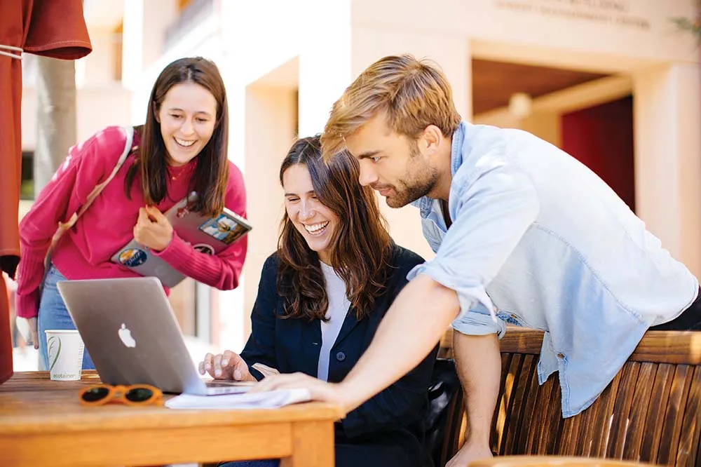 Three GSB students working together outside over a laptop.