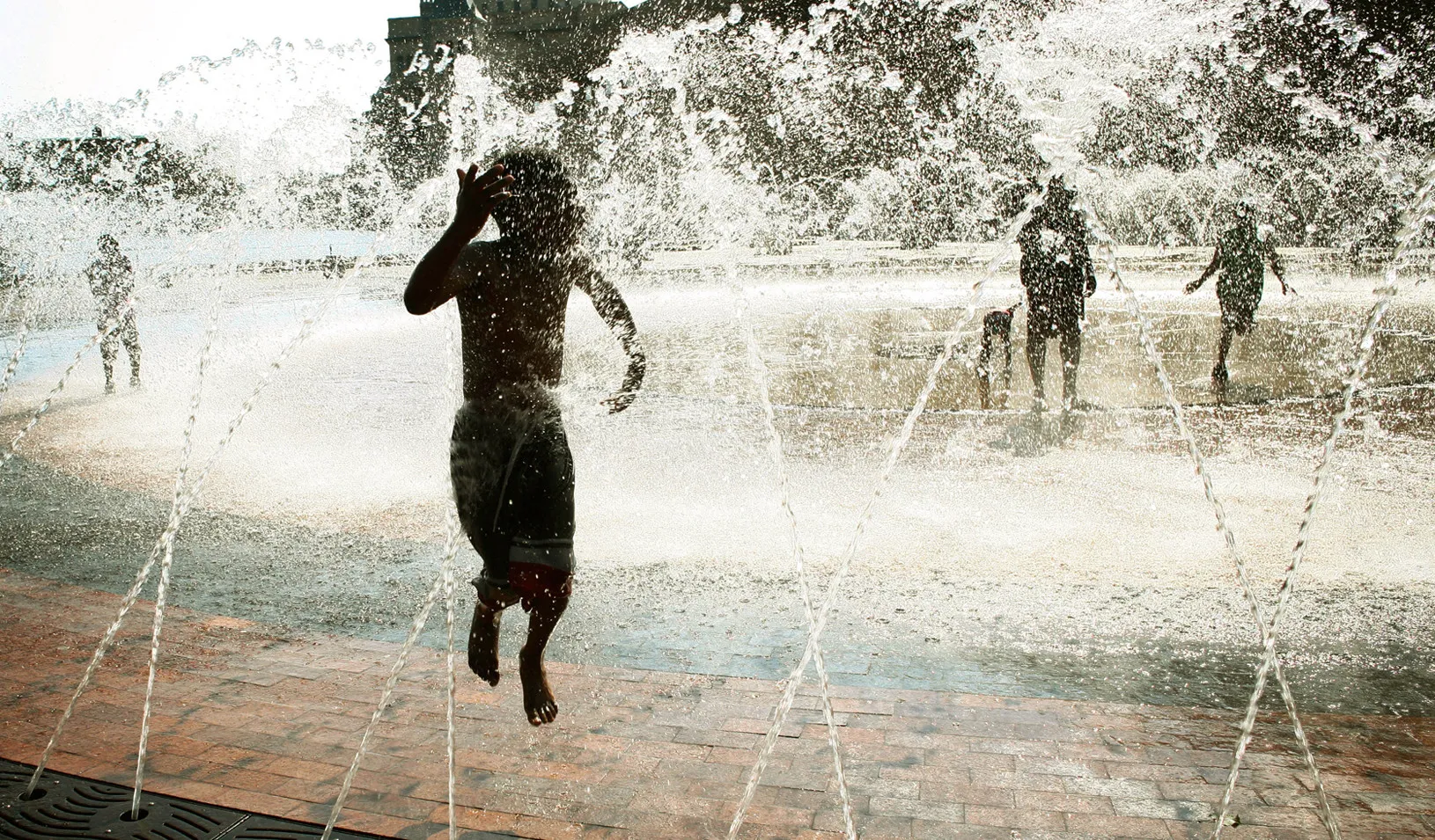 A little boy jumps through a fountain on a hot summer day. (Reuters photo by Brian Snyder )