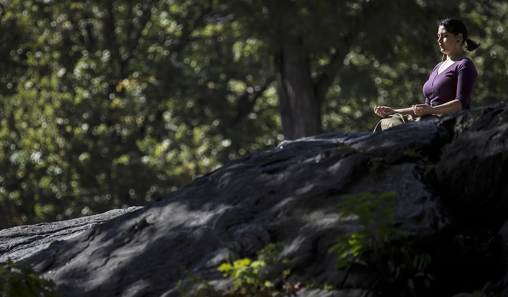 A woman sits on a rock in the mid-afternoon sun and meditates in Central Park. | Reuters/Carlo Allegri
