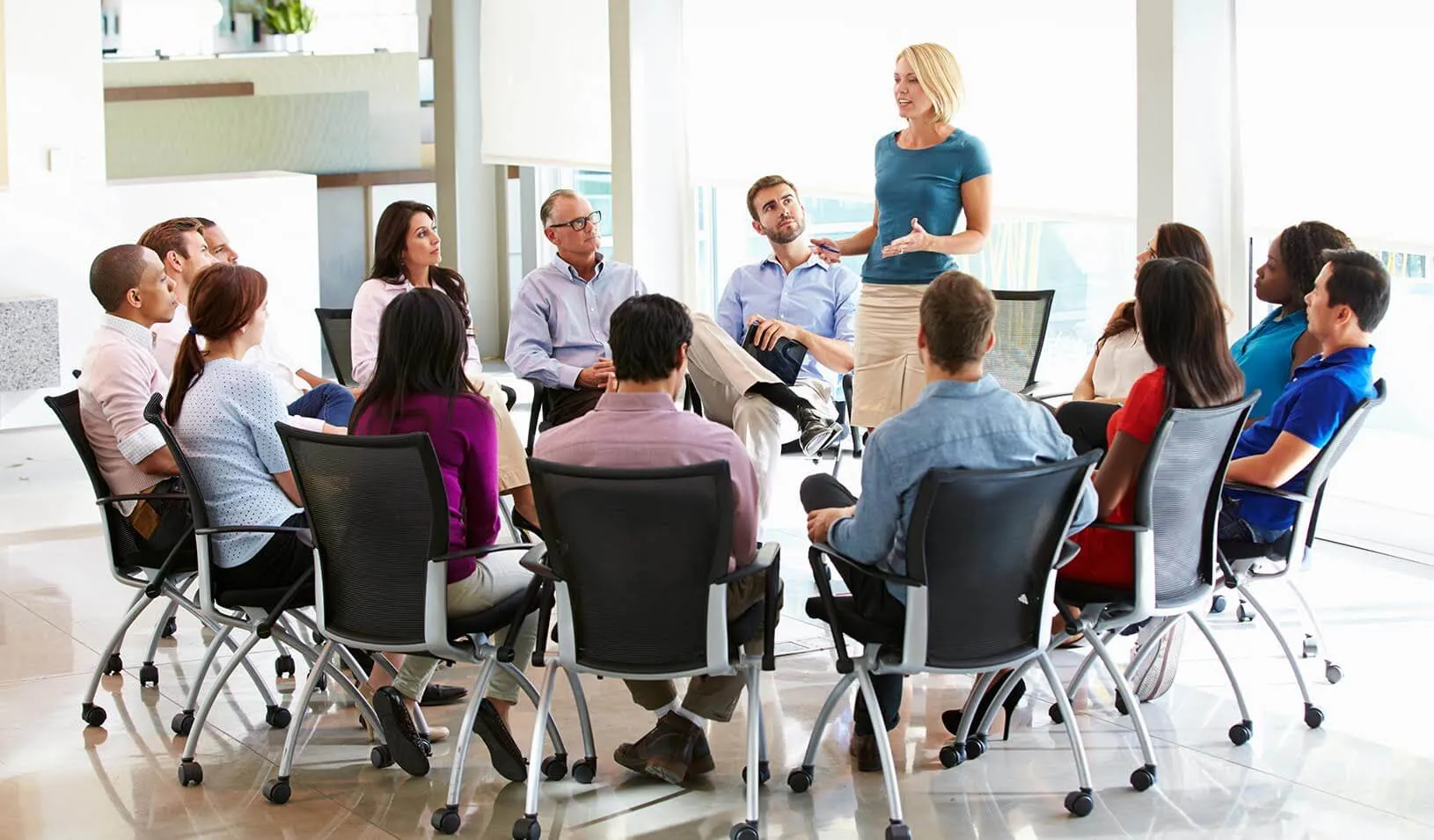 A circle of workers listening to a woman speaker | Adobe Stock