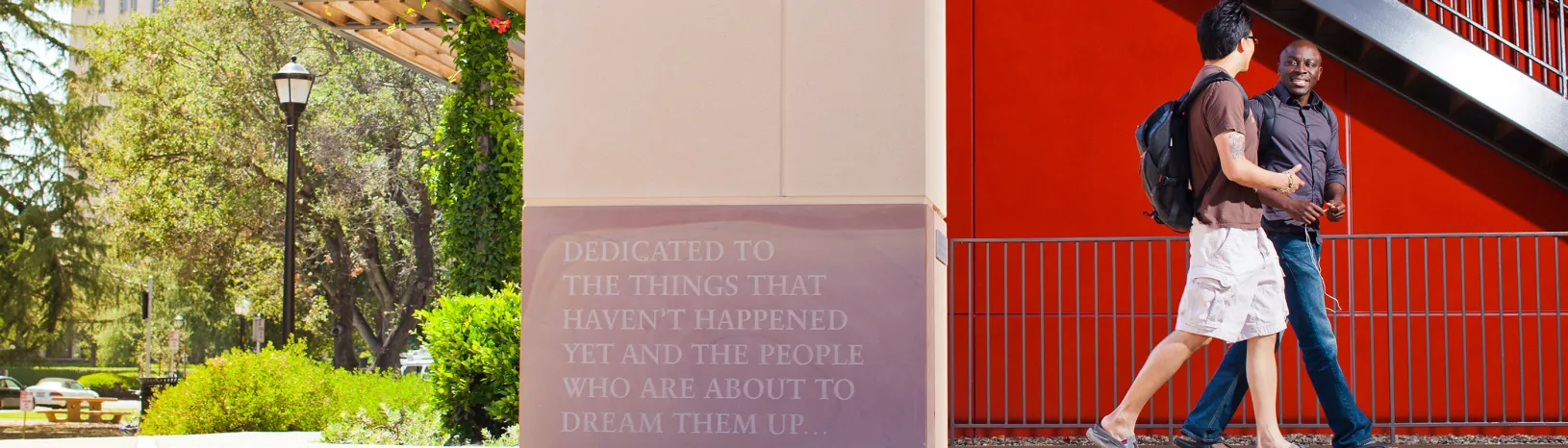 Two students walking by a plaque that reads, “Dedicated to the things that haven’t happened yet and the people who are about to dream them up…”