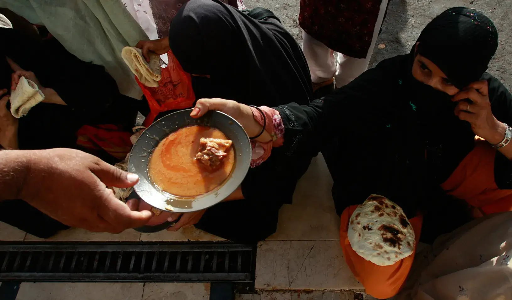 A woman handing a bowl of food to someone else. | Reuters/Athar Hussain