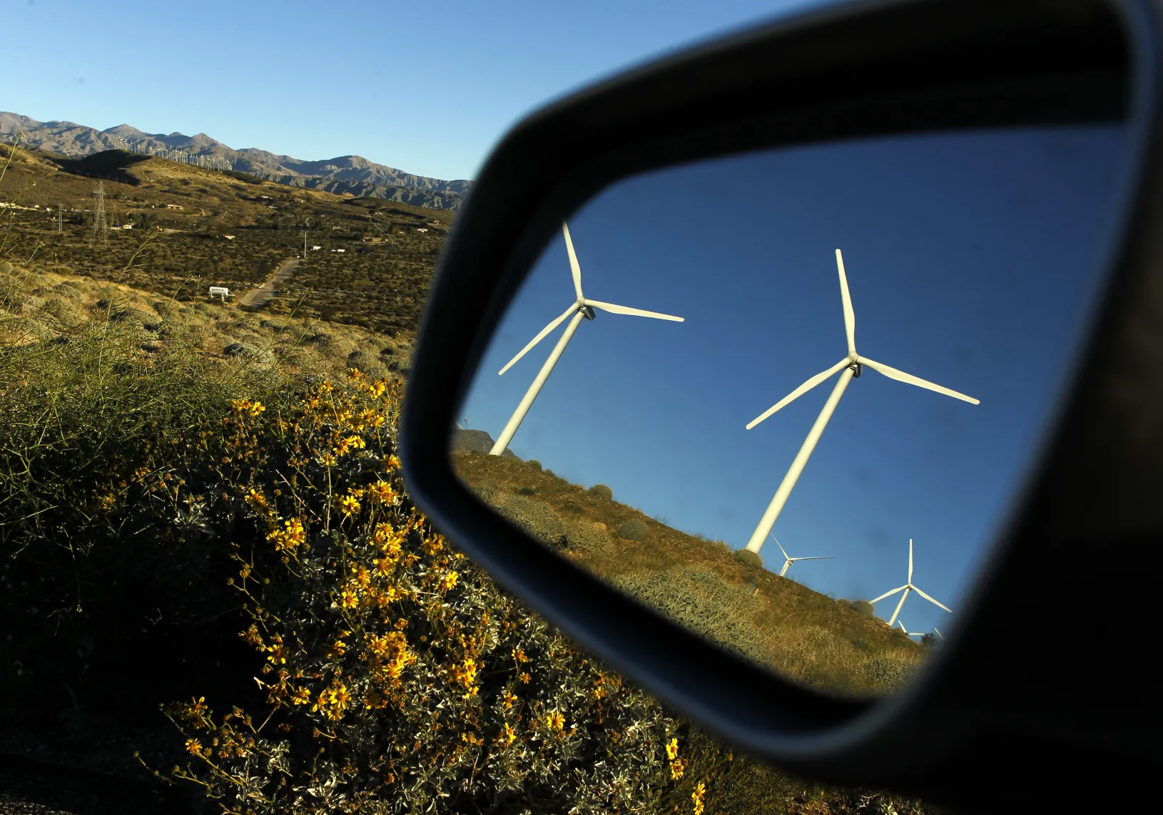 Windmills are reflected in a car mirror at a wind farm.
