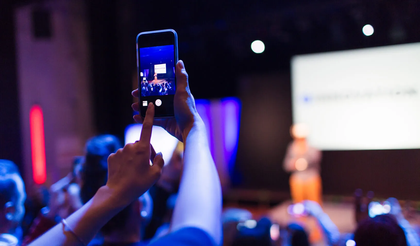 An audience member takes a photo of someone presenting on stage. Credit: iStock/Django