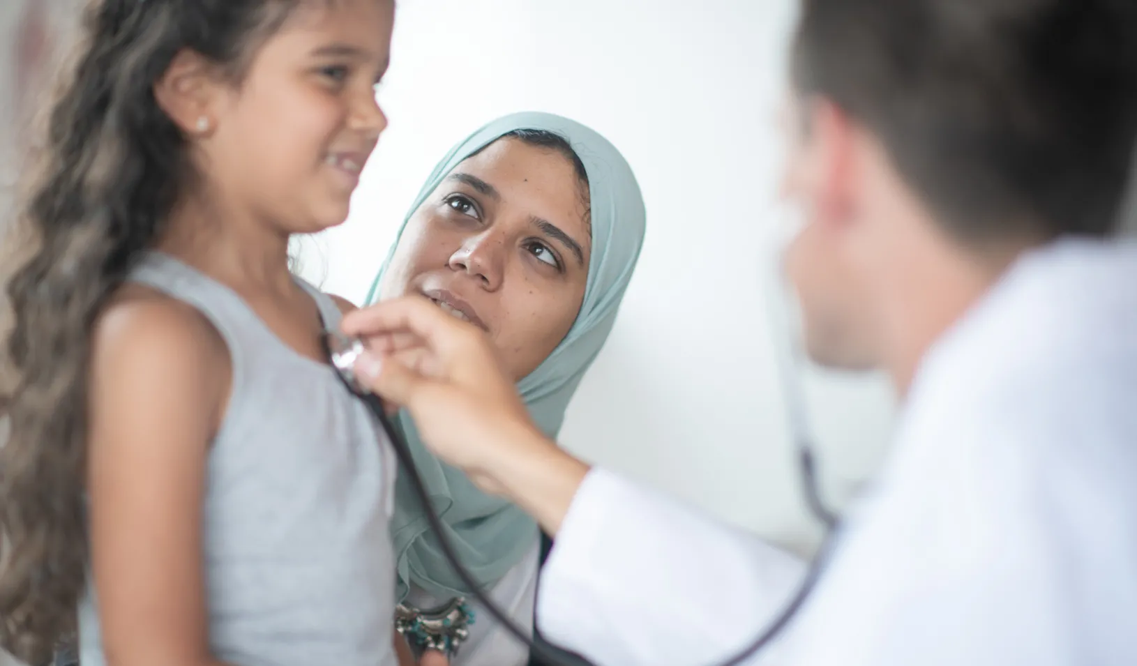 A Muslim girl and her mother are at the hospital. A male doctor is checking the girl's heartbeat. Credit: iStock/FatCamera