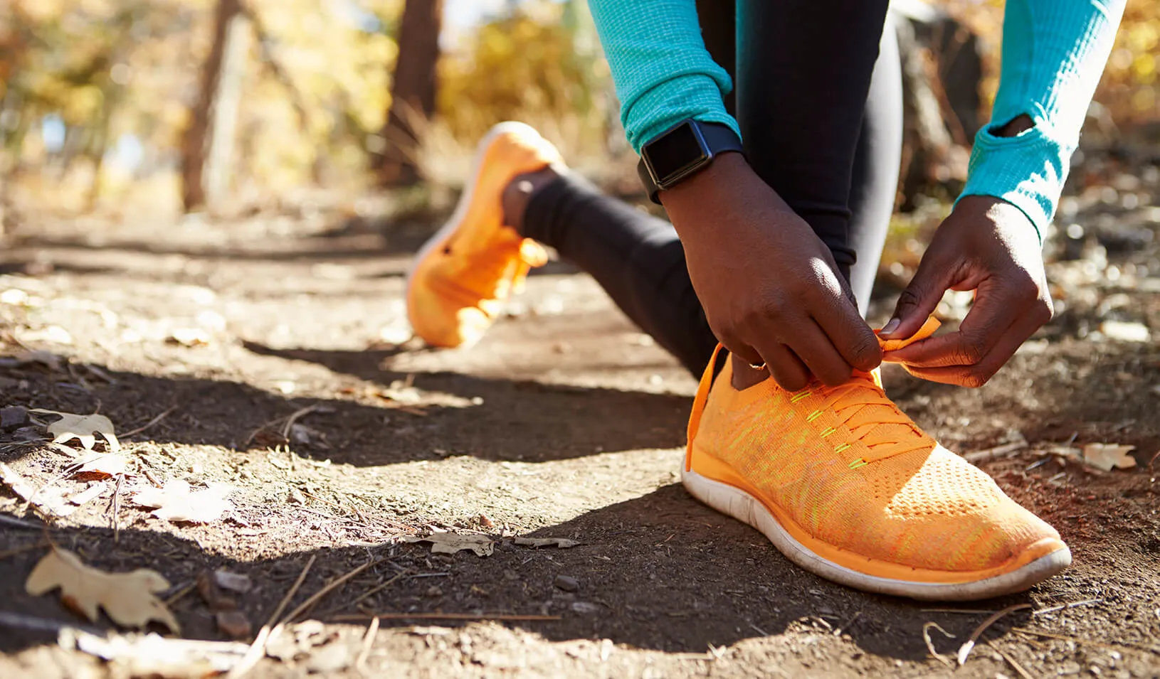 A woman runner wearing a fitness tracker stops to tie her shoe | iStock/monkeybusinessimages