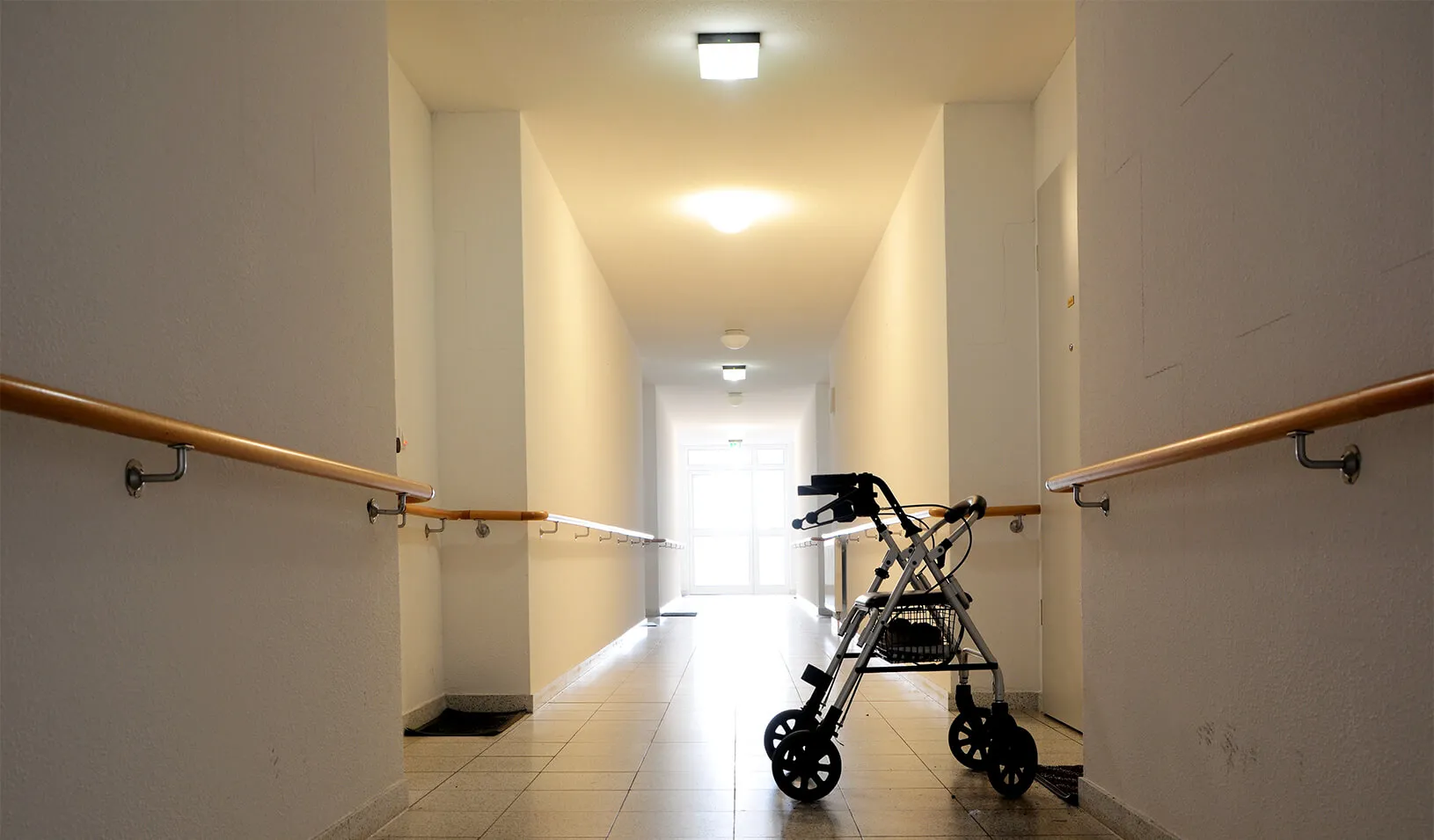 A walker is left behind in the empty hallway of an eldercare facility