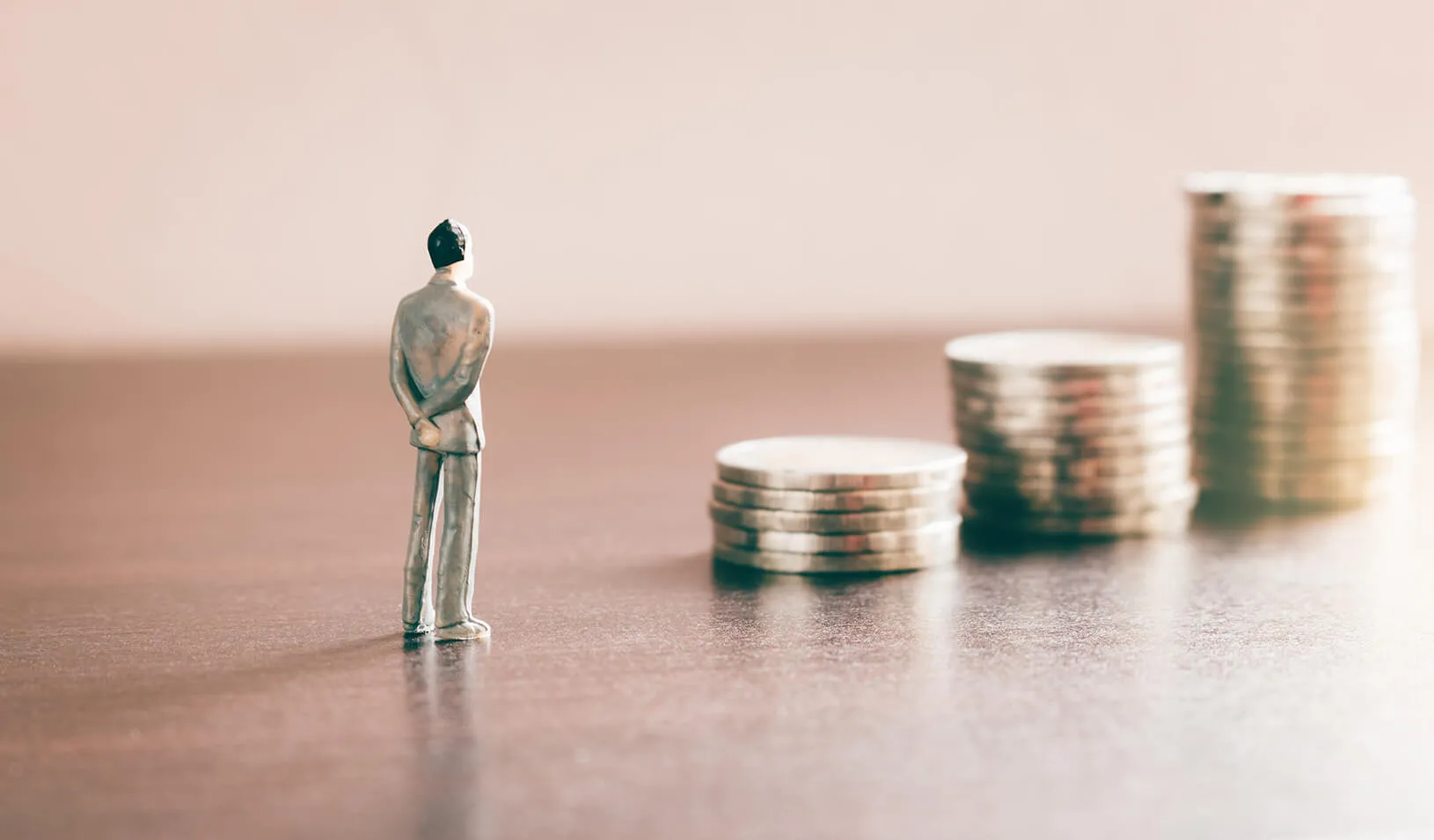 A small figure stands facing 3 piles of coins, in increasing value | iStock/wutwhanphoto