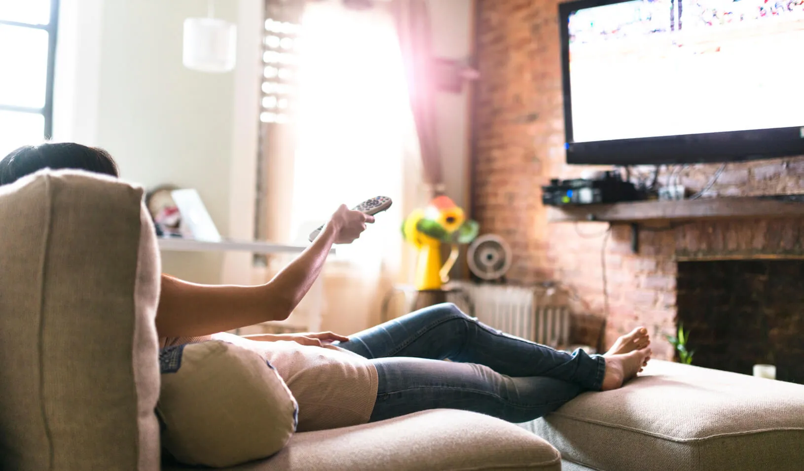 A woman uses the remote to change the channel on the TV. Credit: iStock/franckreporter