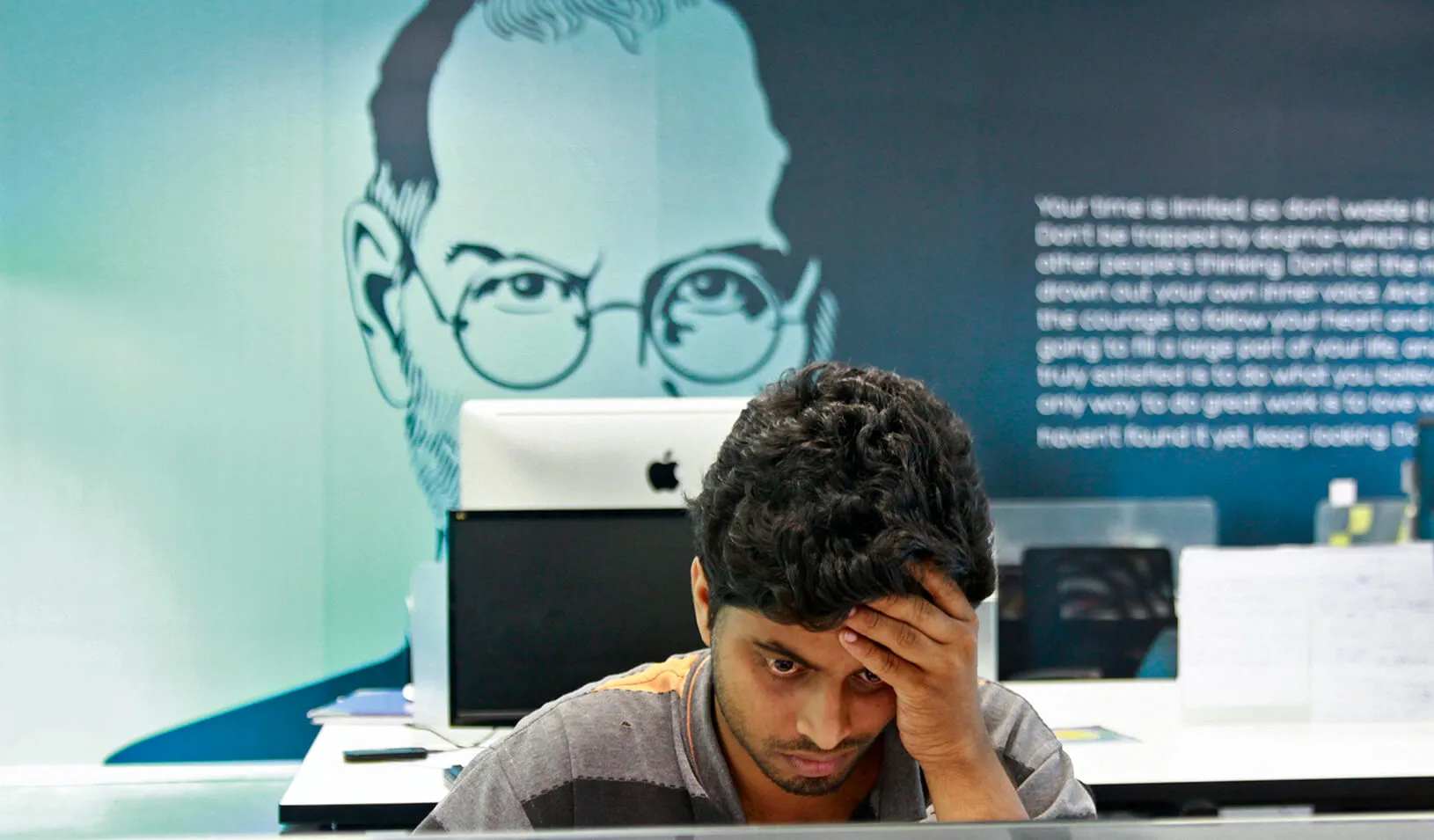 An employee works on a computer terminal against the backdrop of a picture of late Apple cofounder Steve Jobs at the Startup Village in Kinfra Hi-Tech Park. Credit: Reuters/Sivaram V