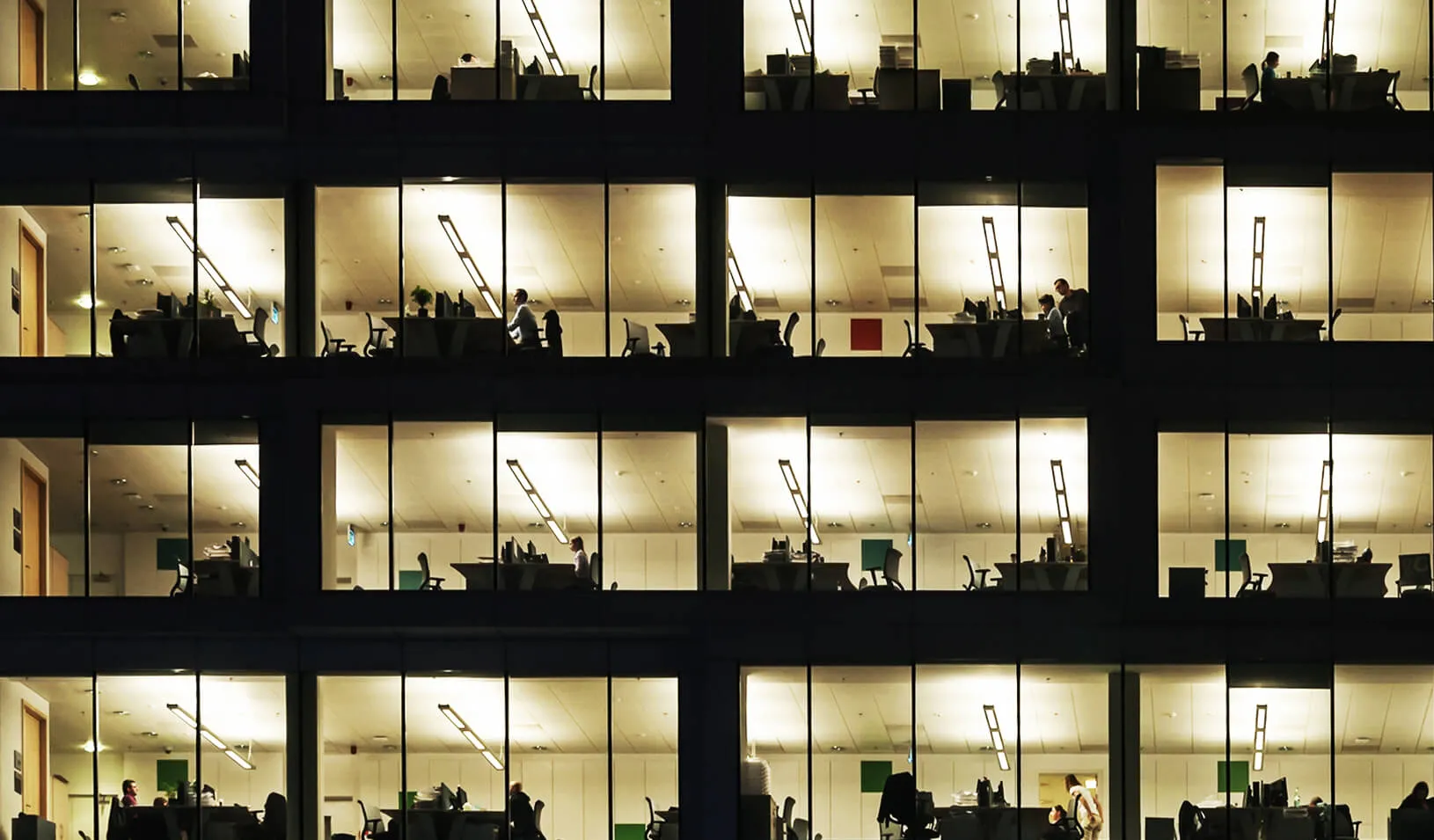 An office building at night showing people working late | iStock/Kilhan