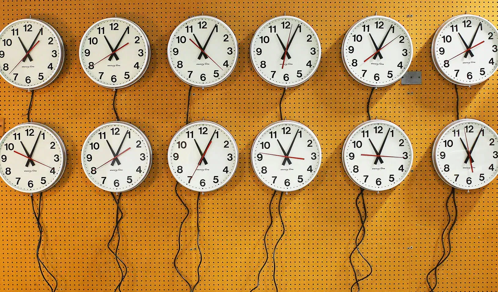 Twelve wall clocks close together. |