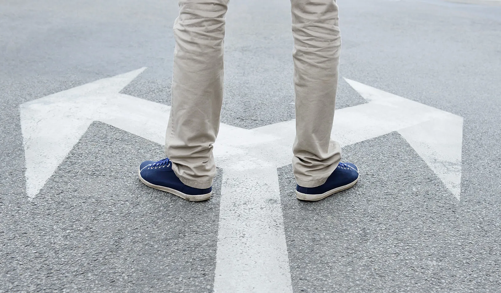 Person standing on directional arrows. | iStock/Olaser