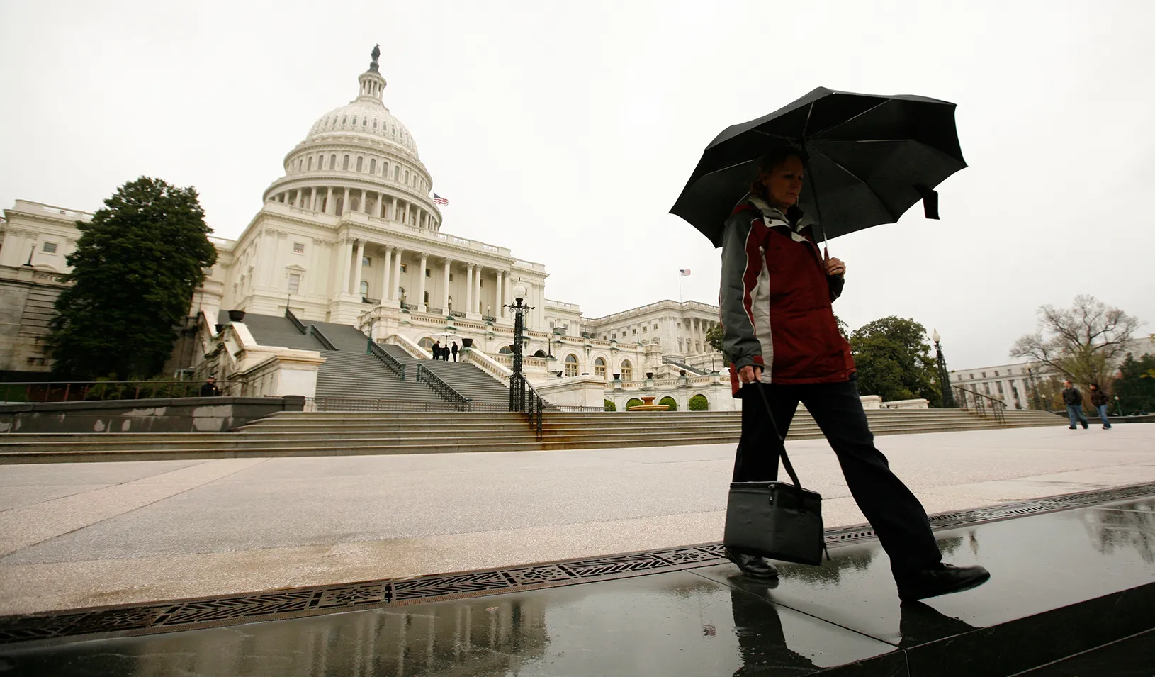 Man with an umbrella walking in front of the Capital Building