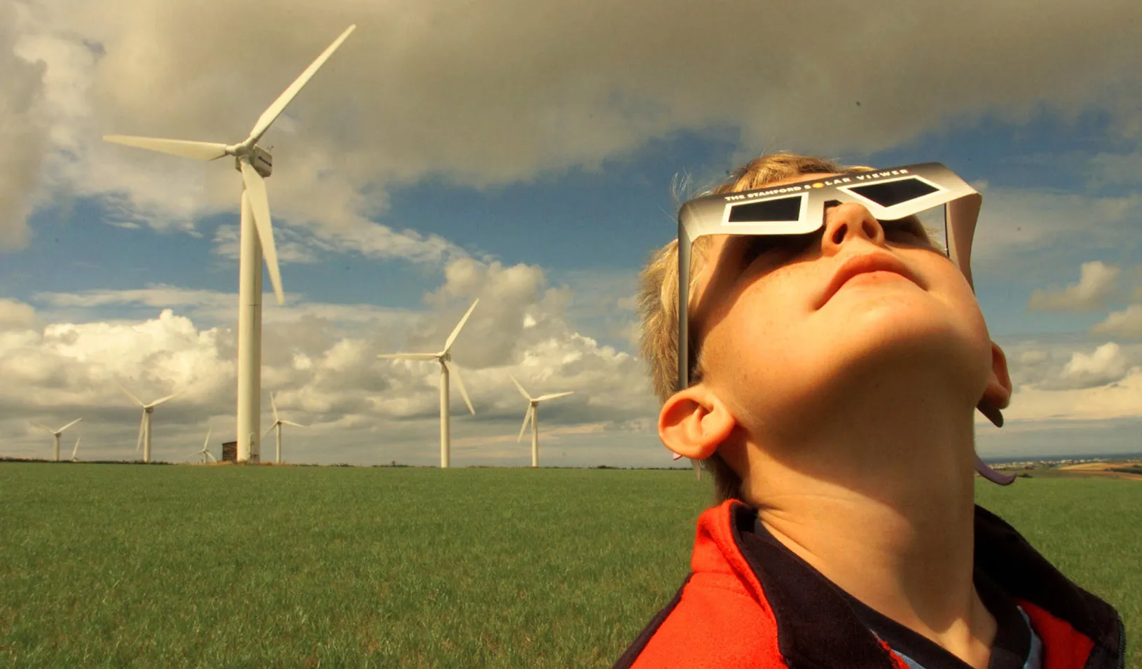 Boy wearing eclipse viewing glasses near a wind farm