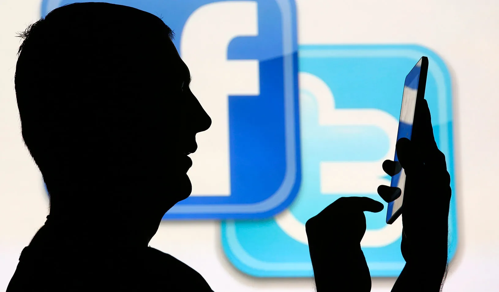 A silhouette of a man in front of the Twitter and Facebook logos