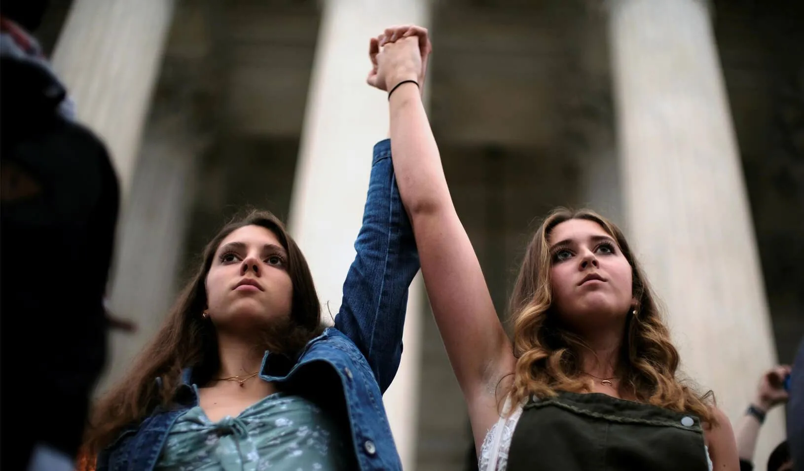 Annabella Helman of Indianapolis, Indiana, and Olivia McAuliffe of McLean, Virginia join hands as other protesters overrun the steps of the U.S. Supreme Court as Brett Kavanaugh is sworn in as an Associate Justice. Credit: Reuters/James Lawler Duggan