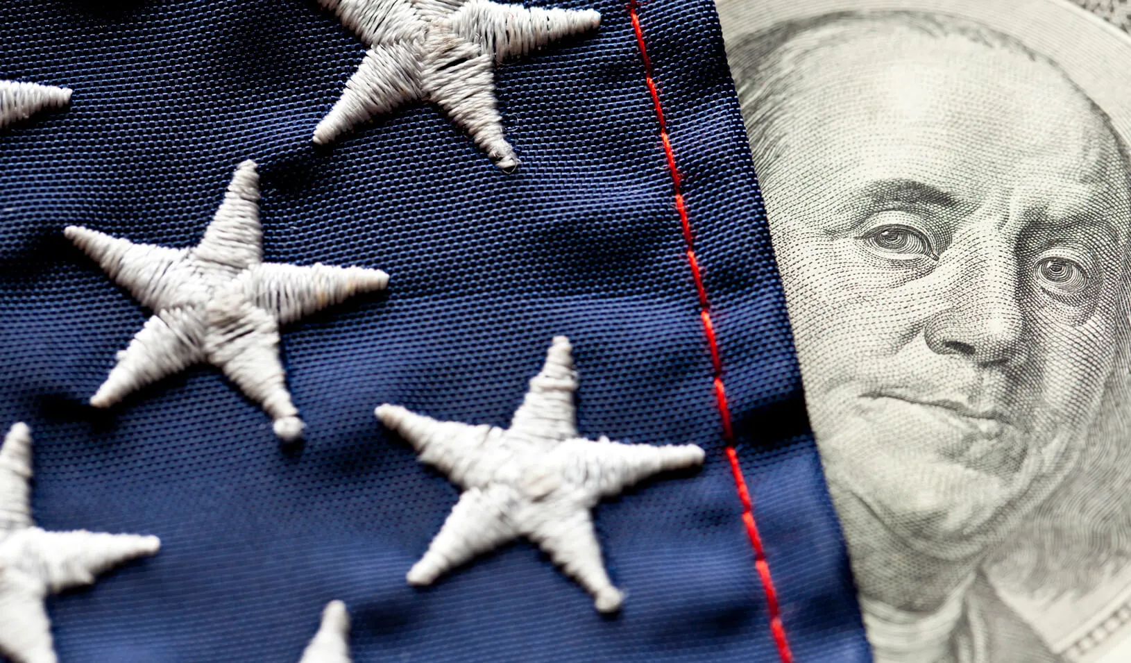 A photo illustration of the face of George Washington on the dollar bill peeking out from behind the U.S. Flag. Credit: iStock/Bill Oxford