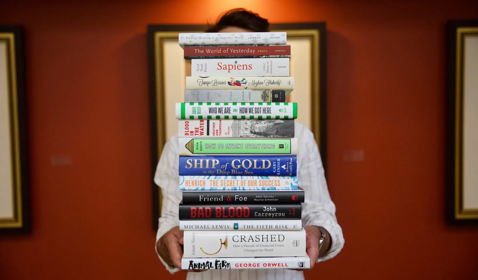 A person holds tall stack of books in a library. Credit: Allison Felt