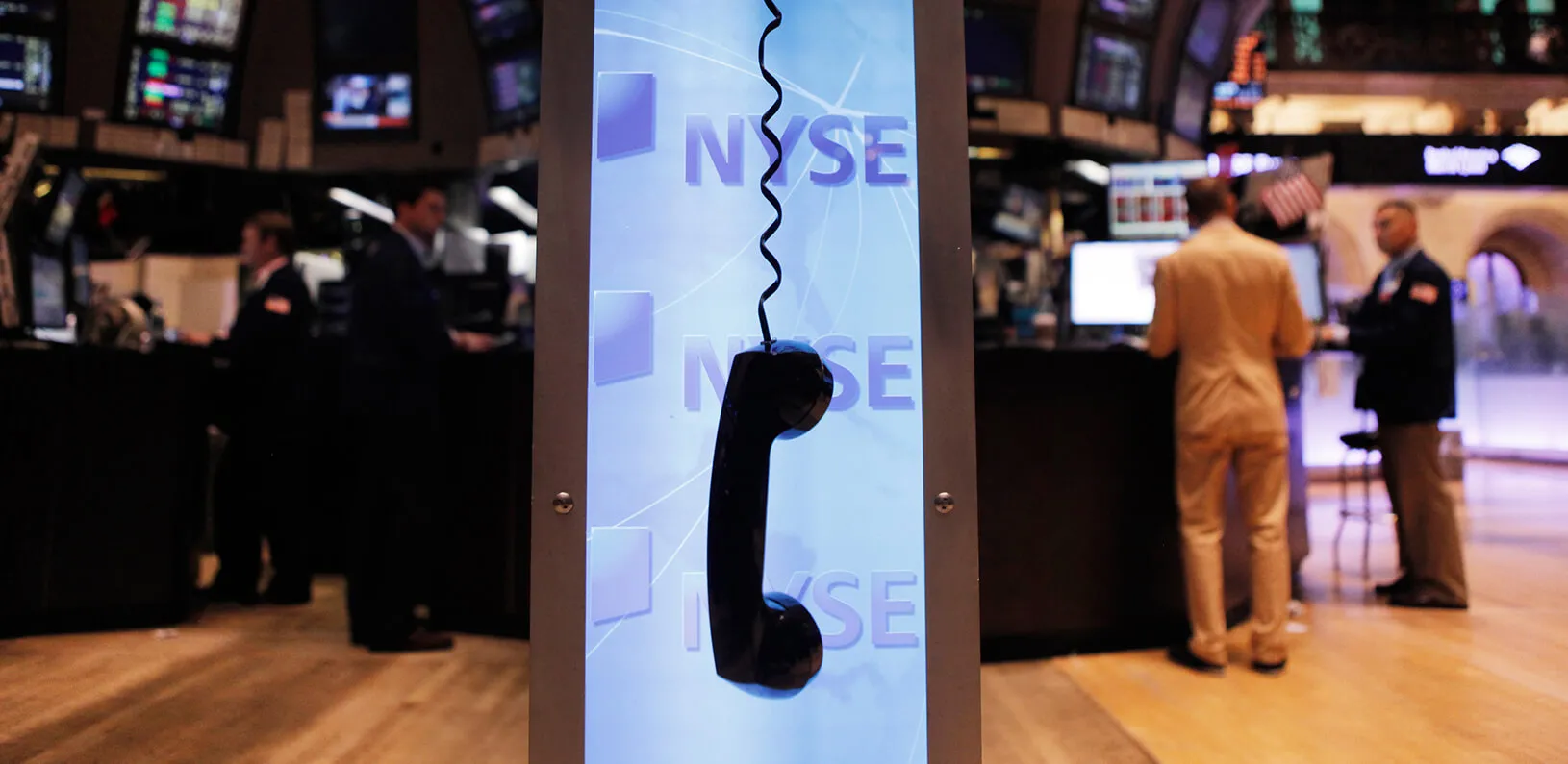 Telephone receiver hanging by its cord in front of the NYSE logo