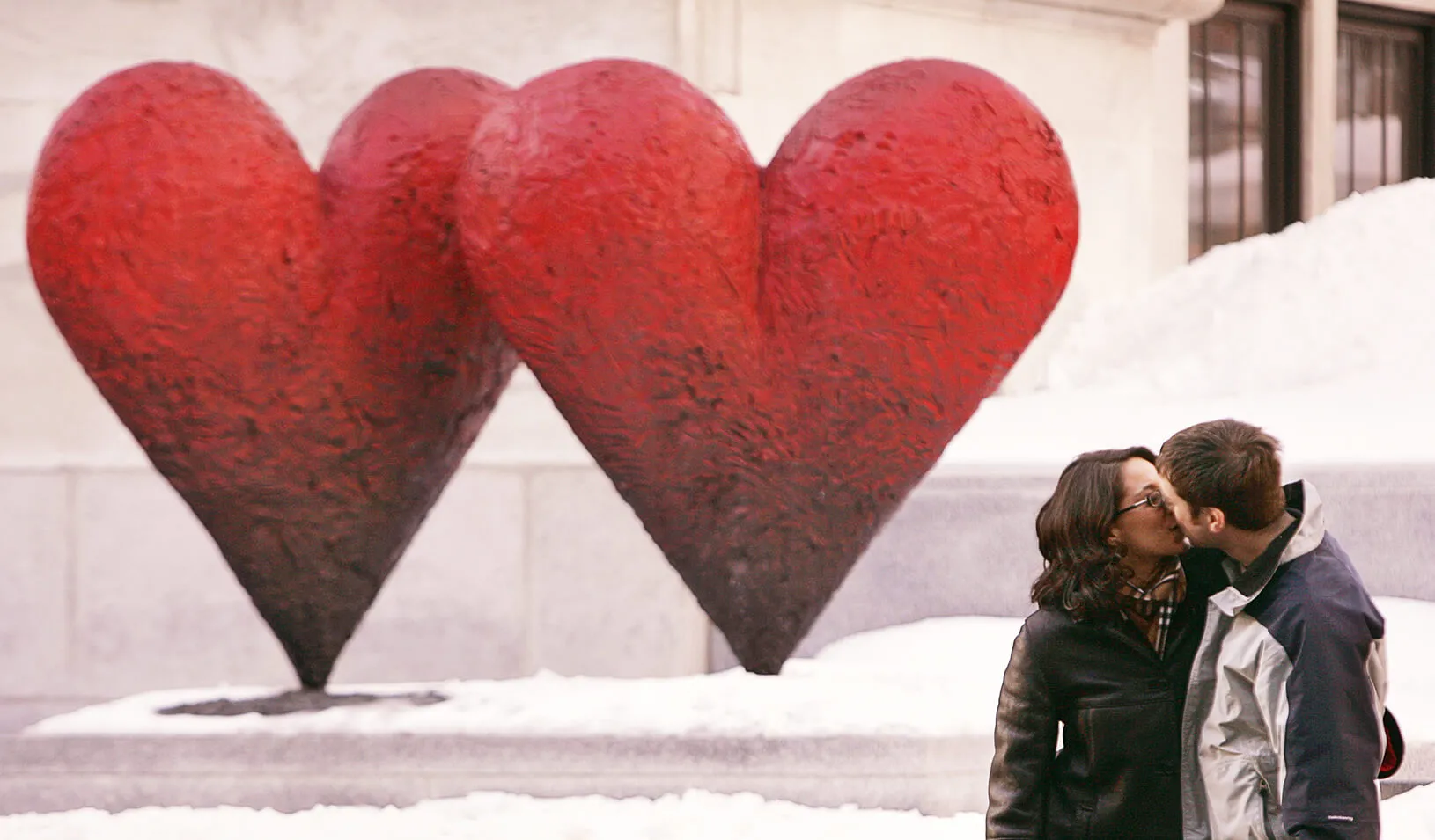 Couple kisses in front of a heart-shaped sculpture