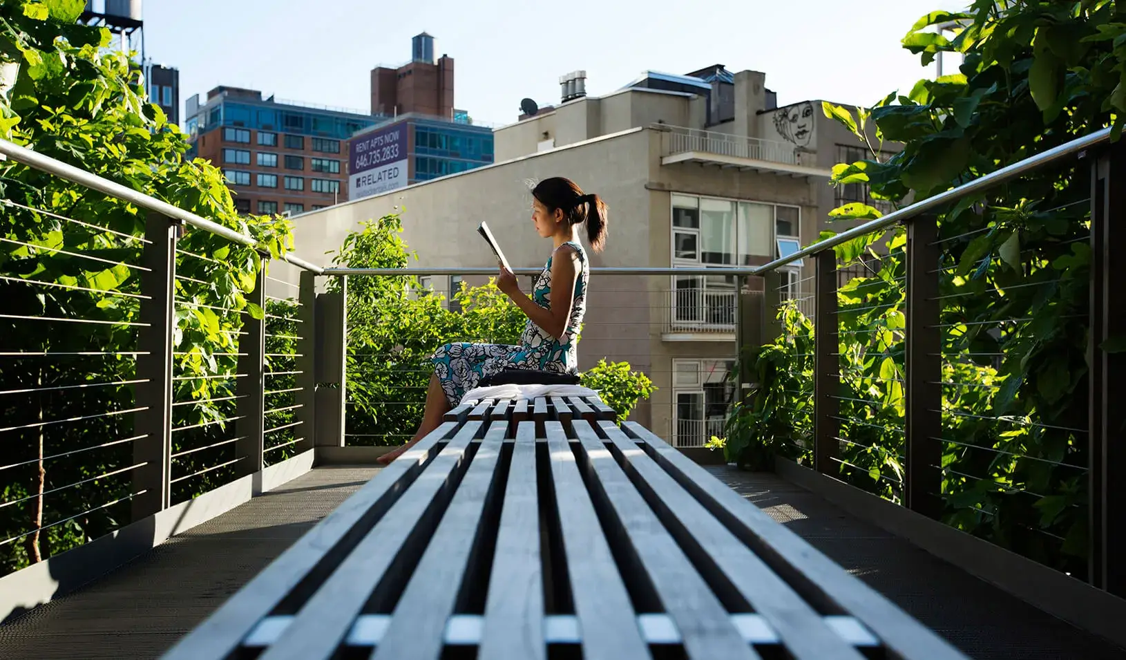 A woman uses the late afternoon sun to read while sitting on the High Line park in New York