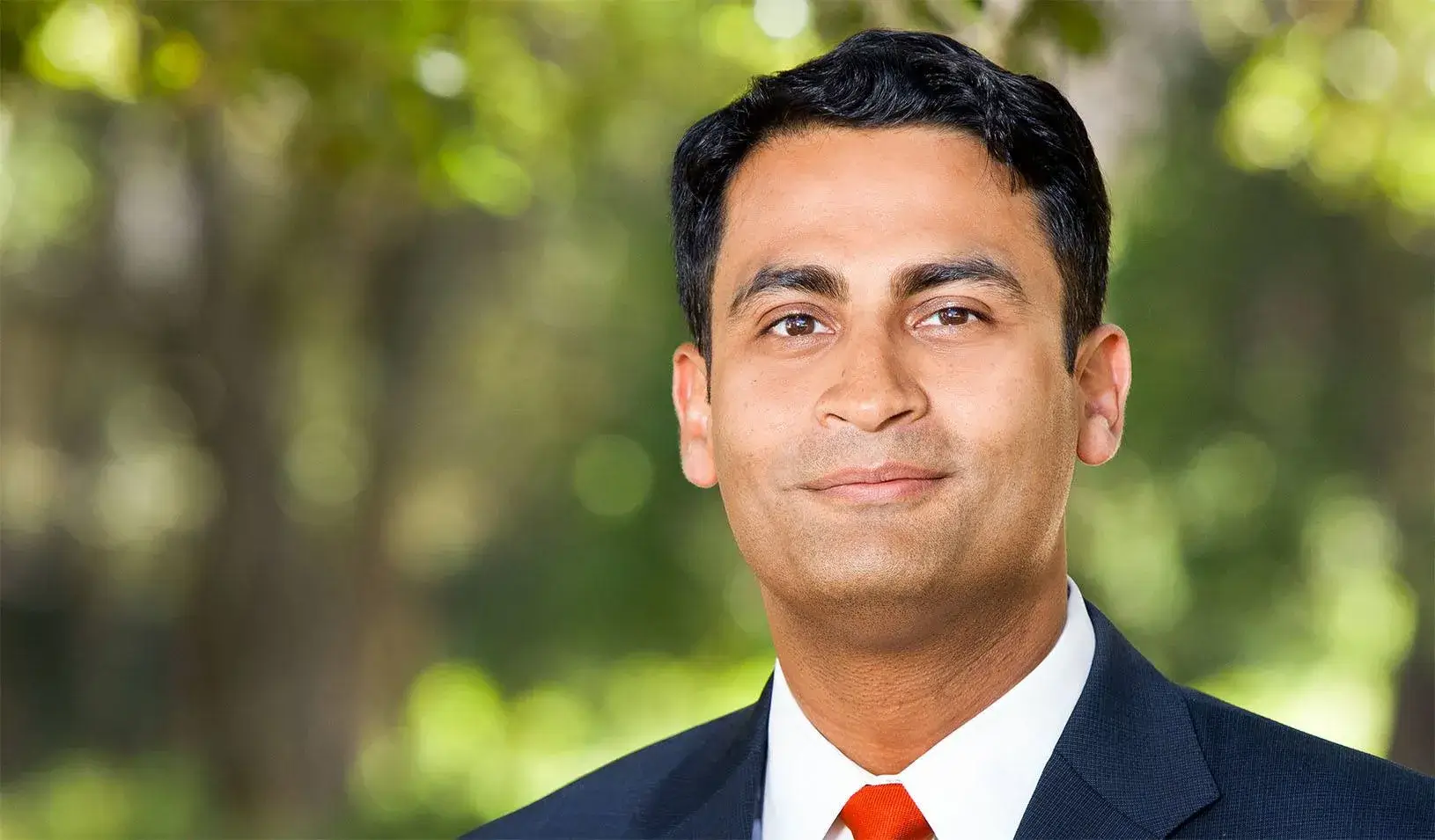 Saumitra Jha smiling outdoors in front of a green background. Credit: Nancy Rothstein.