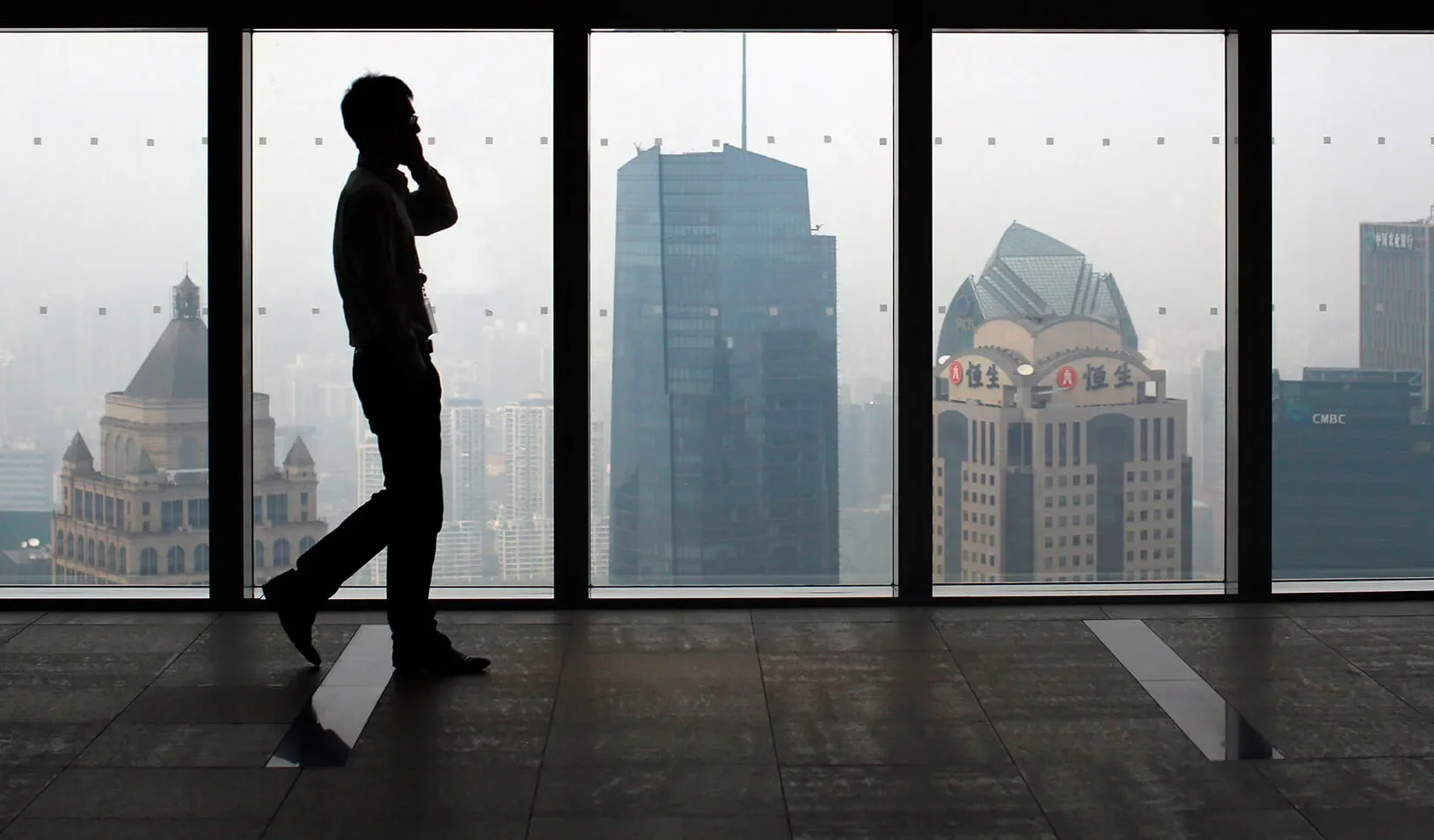A man talks on a mobile phone as he walks past the view of the Shanghai skyline. | Reuters/Carlos Barria