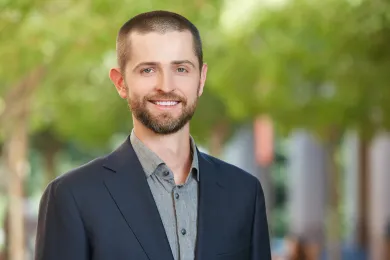 Jonathan Atwell outdoors, smiling in front of green foliage.