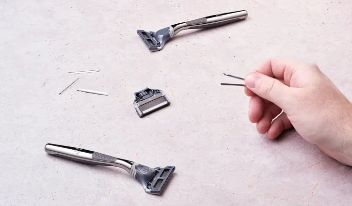 Top down photo of razors and razor blades on a white surface, and a hand coming from the right of the image, holding two razor blades. | Credit: Dan Simmons.