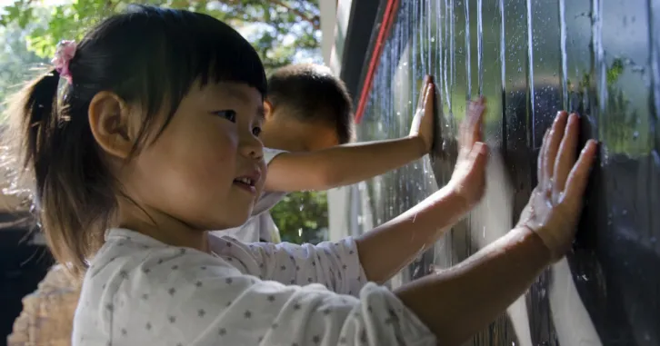 A little girl plays with and learns about water as it trickles down the wall.