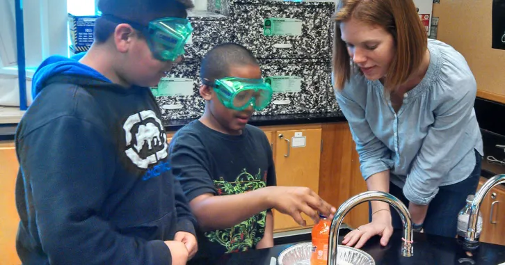 A volunteer and two boys experiment in a classroom.