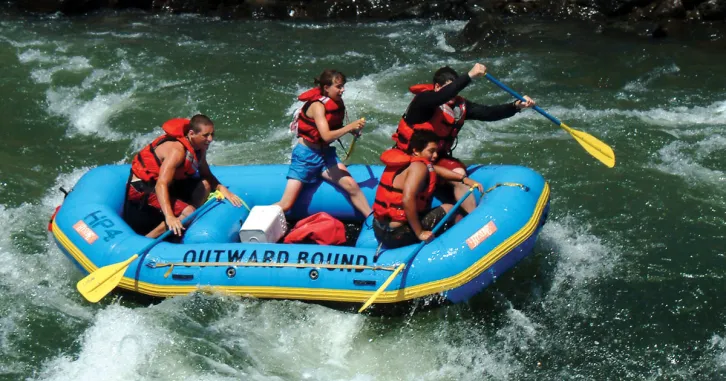 Four young adults paddle down a rapid in an Outward Bound raft.