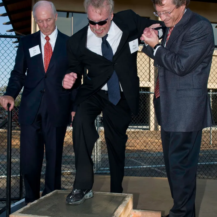 Dean Robert Joss (left) and Provost John Etchemendy (right), give Phil Knight, MBA '62, a hand putting his shoe print into concrete