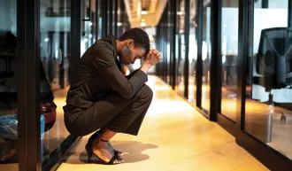 A worried young woman with her head in her hands in the hallway of a modern looking office. Credit:  iStock/FG Trade