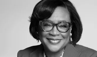 Black and white portrait of Cynt Marshall smiling at the camera wearing glasses and business attire.