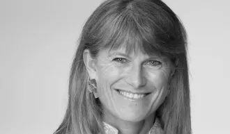 Black and white portrait of Jacqueline Novogratz on a plain background, smiling at the camera.